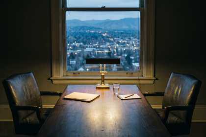 Mesa de reuniones vacía con dos sillas frente a una ventana sobre la ciudad al atardecer